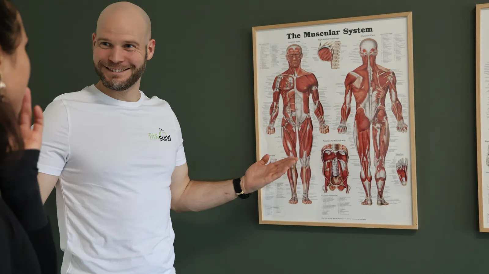 David Brink griner og viser på en plakat over kroppens muskler, mens han forklarer.
